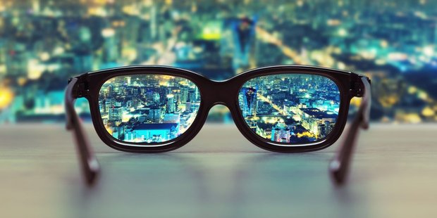Brille mit klarer Sicht auf beleuchtete Stadt. Der Hintergrund ist dafür unscharf.