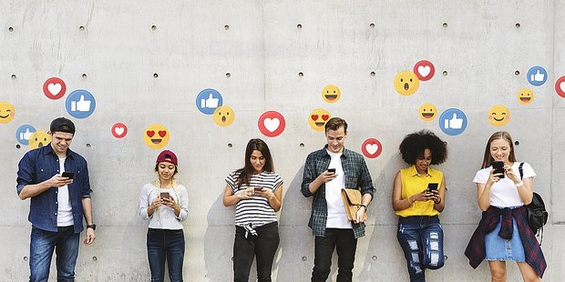 Junge Menschen mit Smartphones umringt von Emoji Symbolen
