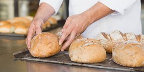 Bäckermeister packt frisches Brot auf ein Backblech mit anderen Broten