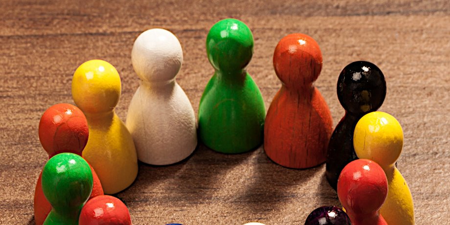 Nahaufnahme verschiedenfarbiger, im Kreis aufgestellter Spielfiguren im Stil der "Mensch ärgere dich nicht"-Figuren