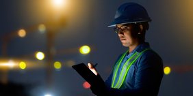 Arbeiter mit Helm und Tablet im Dunkeln mit Lichtpunkten