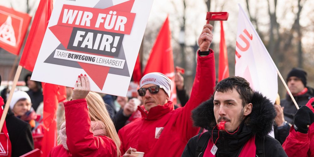 Gewerkschaftsmitglieder demonstrieren mit Fahnen, Trillerpfeifen und Schildern. Auf dem Schild ist zu lesen: Wir für Fair! Tarifbewegung Leiharbeit