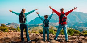 Familie mit Wanderrucksäcken streckt die Arme vor Berg Panorama in die Höhe