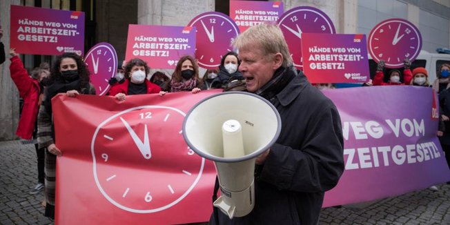 Reiner Hoffmann (DGB-Vorsitzender) mit Megafon bei einem Protest zum Auftakt der nächsten Spitzenrunde der Koalitionsverhandlungen, im Hintergrund Gewerkschafter*innen mit Uhrenschildern und Schildern mit der Aufschrift: "Hände weg vom Arbeitszeitgesetz"