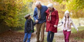 Großeltern spazieren mit Enkelkindern im Wald im Herbst
