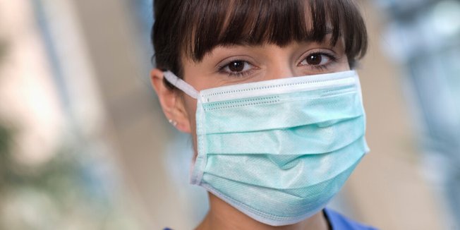 Nahaufnahme von Frau mit Mund-Nasen-Schutz (und blauer Pflegepersonalkleidung)
