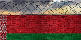 Mauer mit Stacheldraht in den Farben der belarussischen Flagge 