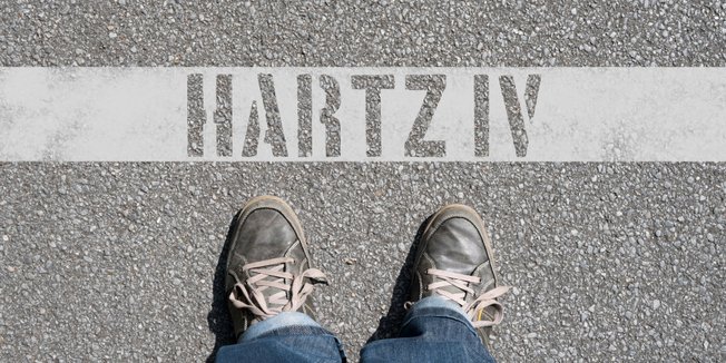 Schuhe stehen auf Asphalt vor Schriftzug "Hartz IV" 