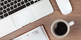 Laptop, Kaffeetasse und Kalender auf einem Holztisch