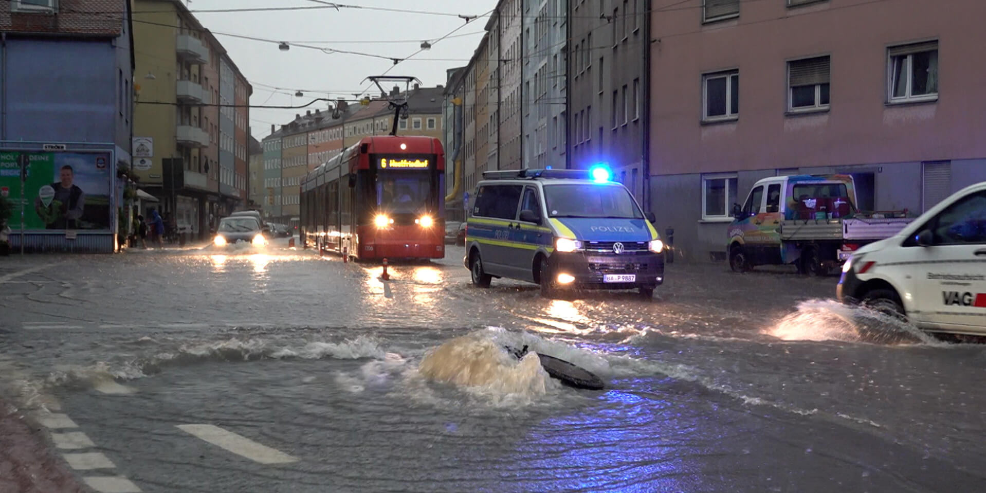 Straßenbahn, Polizeiauto und andere Autos auf einer von Regen überfluteten Straße in einer Stadt