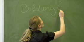 Eine Schülerin schreibt das Wort Bildung an die Tafel.