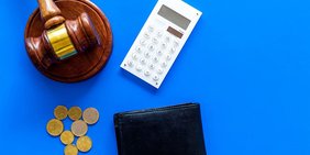 Richterhammer, Münzen, Geldbörse und Taschenrechner auf blauem Grund