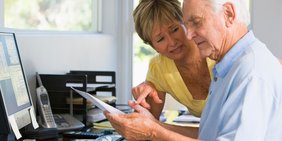 Älterer Mann und ältere Frau im Gespräch während Arbeit vor Bildschirm