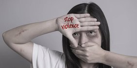 körperlich verletzte Frau in Schutzstellung mit erhobener Hand in der "Stop Violence" steht