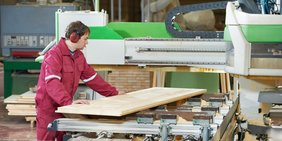Tischler in einer Werkstatt an einer großen Maschine; schiebt Holzplatte entlang der Maschine