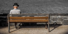 alter Mann sitzt allein auf einer Holzbank