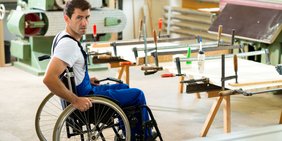 Mann im Blaumann und Rollstuhl in einer Werkstatt