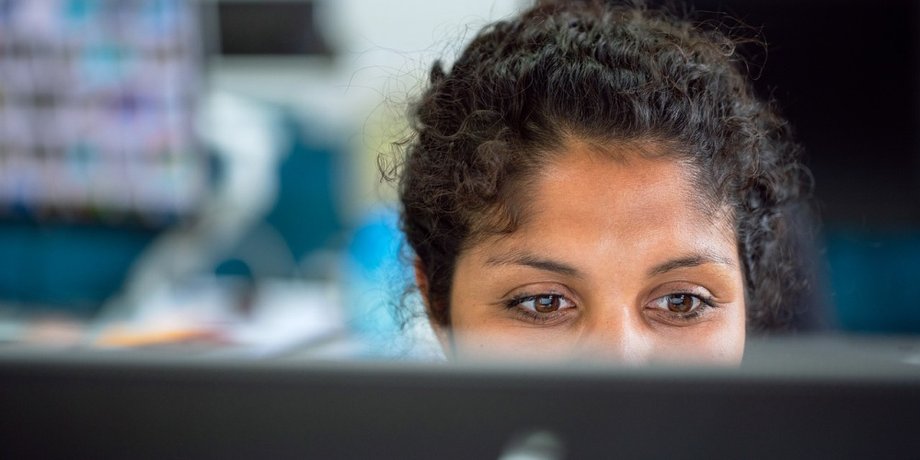 Dunkelhaarige Frau sitzt auf der Arbeit hinter einem Computerbildschirm