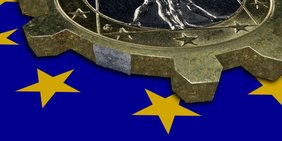Euro Münze in Form eines Zahnrads auf EU-Flagge