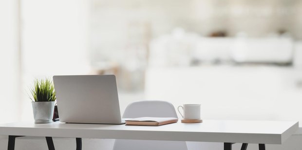 Weißer Tisch mit Laptop, Notizbuch, Kaffeetasse und Topfpflanze