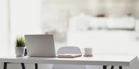 Weißer Tisch mit Laptop, Notizbuch, Kaffeetasse und Topfpflanze