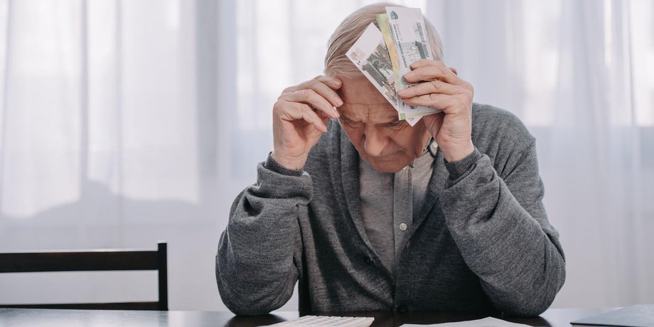 Rentner sitzt mit Geldscheinen am Kopf an Rechnungen