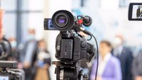Bild einer Kamera, die eine Medienveranstaltung oder Pressekonferenz filmt. 