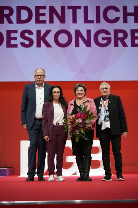 Der frisch gewählte GBV steht nebeneinander auf einer Bühne vor rotem Hintergrund mit der Aufschrift "23. Ordentlicher Bundeskongress". Yasmin Fahimi in der Mitte hält einen bunten Blumenstrauß, alle lächeln.