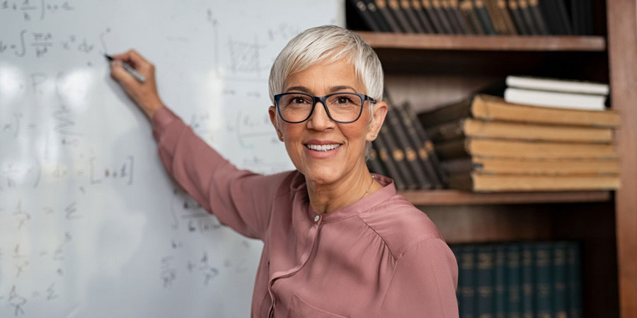 Portrait einer Lehrerin, die in die Kamera lächelt, während sie auf einem Whiteboard etwas schreibt.