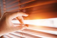 Jemand spreizt eine Jalousie mit den Fingern, Sonne scheint hindurch
