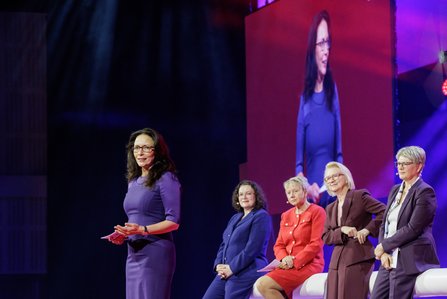 Yasmin Fahimi im violetten Kleid steht links im Vordergrund und spricht, vier weitere Frauen – Andrea Nahles, Inken Gallner, Monika Schnitzer, Gundula Roßbach – sitzen auf weißen Sesseln, im Hintergrund eine große Leinwand.