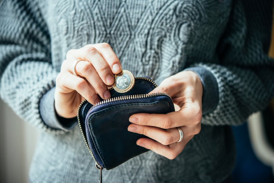 Frau hat eine Münze in einer Hand und will diese in ein Portemonnaie, welches sie in der anderen Hand hält, einstecken.