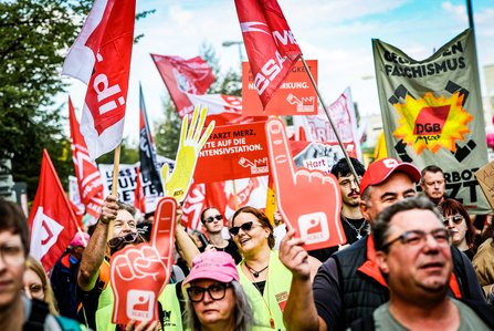 Demonstrierende halten Gewerkschaftsfahnen und rote Schaumstoffhände hoch; rechts ist ein Banner der DGB-Jugend gegen Faschismus zu sehen.