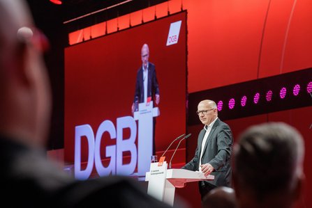 Kai Wegner, Regierender Bürgermeister von Berlin, im dunklen Anzug und mit Brille am Rednerpult vor rotem Hintergrund mit großem DGB-Logo.