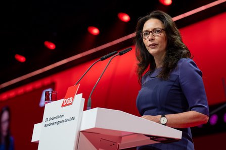 Yasmin Fahimi im violetten Kleid spricht konzentriert am Rednerpult, hinter ihr ein roter Hintergrund.