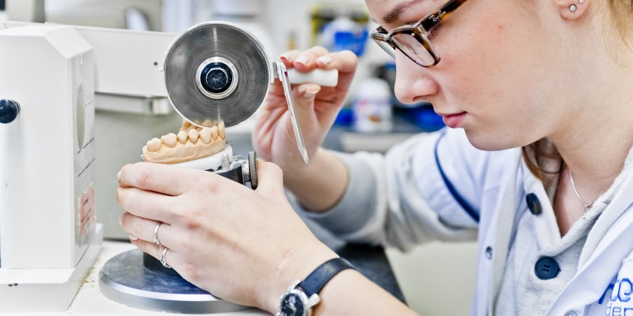 Eine Frau mit Arbeitskittel und Schutzbrille arbeitet an einem Gipsabdruck eines Gebisses