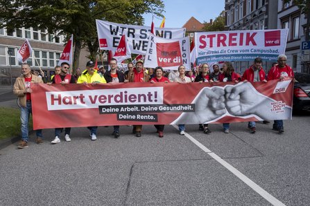 Beschäftigte tragen beim DGB-Aktionstag in Kiel ein Banner mit der Aufschrift „Hart verdient! Deine Arbeit. Deine Gesundheit. Deine Rente.“