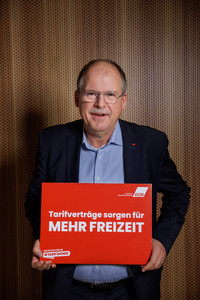 Foto von Stefan Körzell, der ein Plakat hält mit der Aufschrift "Tarifverträge sorgen für mehr Freizeit"