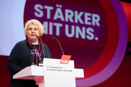 Eine Frau mittleren Alters mit kurzen grauen Haaren und Brille spricht am Rednerpult. Sie gestikuliert mit der rechten Hand. Im Hintergrund der Schriftzug "Stärker mit uns".
