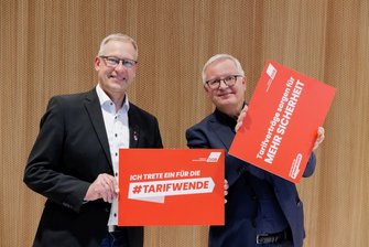 Foto von Andreas Luttmer-Bensmann und Stefan Eirich (Katholische Arbeitnehmer-Bewegung), die jeweils ein Plakat halten mit den Aufschriften "Ich trete ein für die #Tarifwende" und "Tarifverträge sorgen für mehr Sicherheit".