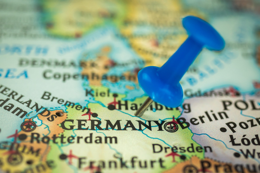 Nahaufnahme von einer Deutschlandkarte in einem Atlas mit einem blauen Pin, der in auf Deutschland steckt.