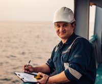 Deckoffizier an Deck eines Offshore-Schiffes oder -Schiffes, der persönliche Schutzausrüstung trägt. Er füllt Checkliste. Papierkram auf See