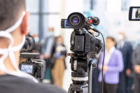 Bild einer Kamera, die eine Medienveranstaltung oder Pressekonferenz filmt. 