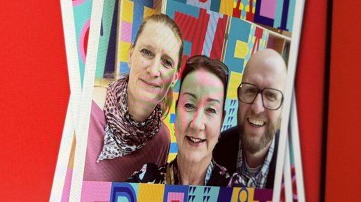 Das Bild zeigt einen Bildschirm, auf dem mehrere übereinanderliegende Selfies abgebildet sind. Die oberste Karte trägt die Wörter "Vielfalt Freiheit" in bunten, stilisierten Buchstaben. Der Hintergrund des Bildschirms ist rot, und links neben dem Bildschirm befindet sich Text, der Informationen über die Nutzung eines QR-Codes für den Zugang zu einer Online-Galerie und die Möglichkeit zur Teilnahme auf Social Media bietet. Die Gestaltung ist lebendig und auffällig, um das Thema Vielfalt und Gemeinschaft zu betonen. Der Text "Gemeinsam stark" ist ebenfalls sichtbar und unterstreicht die Botschaft der Einheit und Stärke.