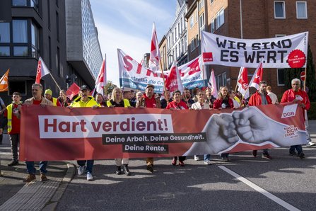Beschäftigte tragen beim DGB-Aktionstag in Kiel ein Banner mit der Aufschrift „Hart verdient! Deine Arbeit. Deine Gesundheit. Deine Rente.“